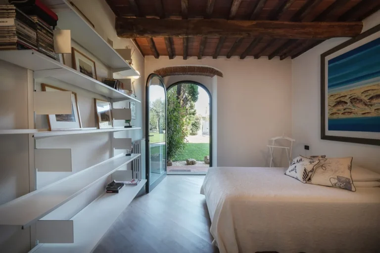 Bedroom of the ARABELLA villa apartment with wooden beams and an arched French door open to the garden