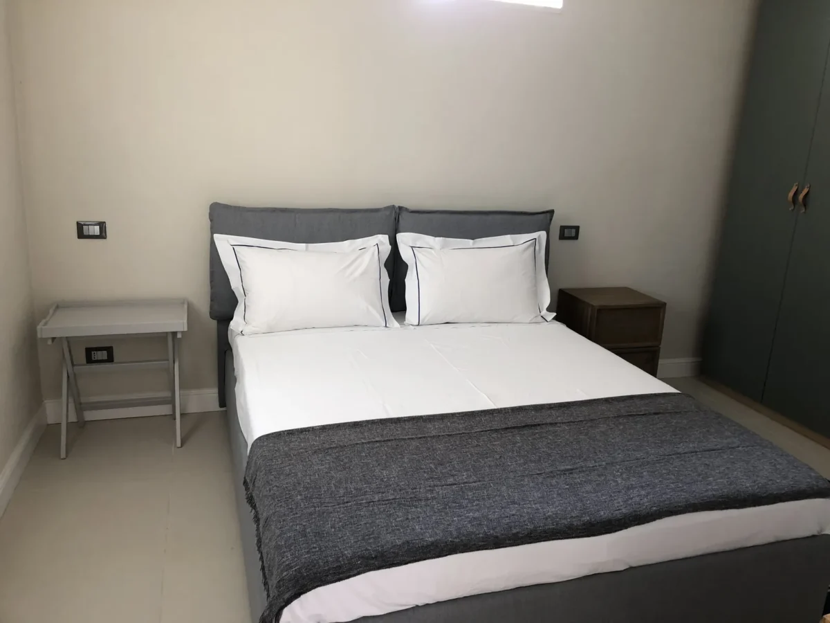 Double bedroom of the ARA garden apartment with upholstered grey headboard and white linen