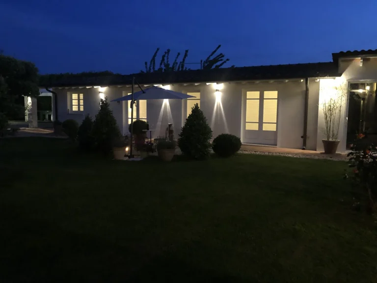 The garden apartment ARA lit up at dusk, with parasol and topiary