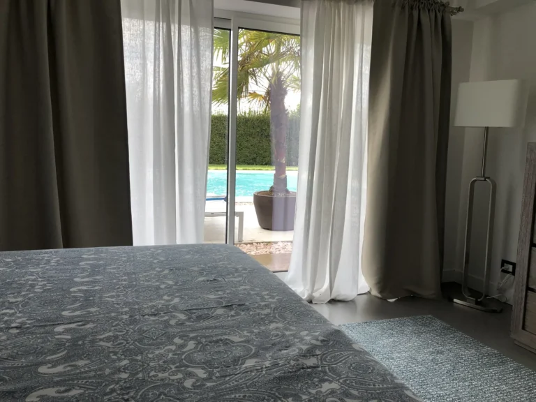 View from the bed through the glass door to a palm tree and the pool