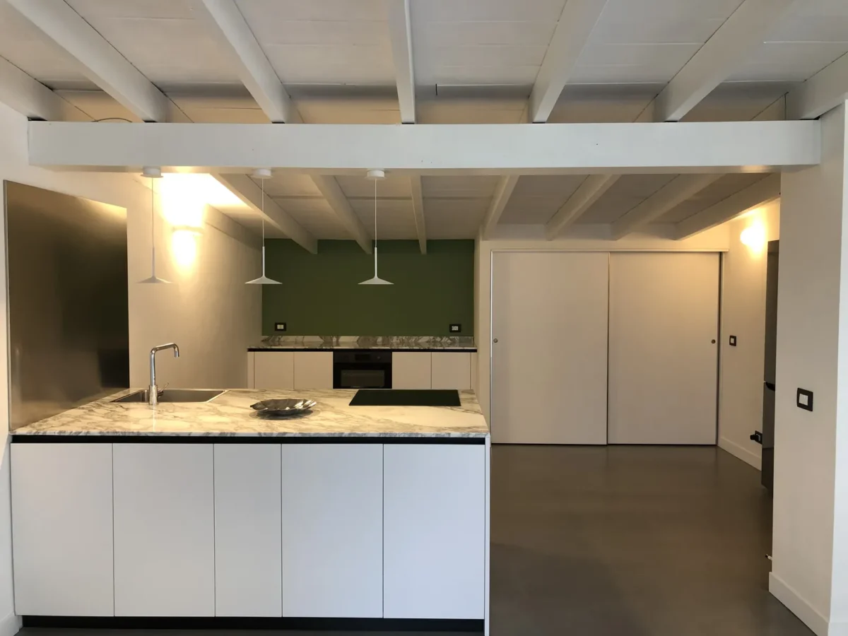Kitchen of the BELLA apartment in Pietrasanta with white marble island, pendant lamps and sage-green wall