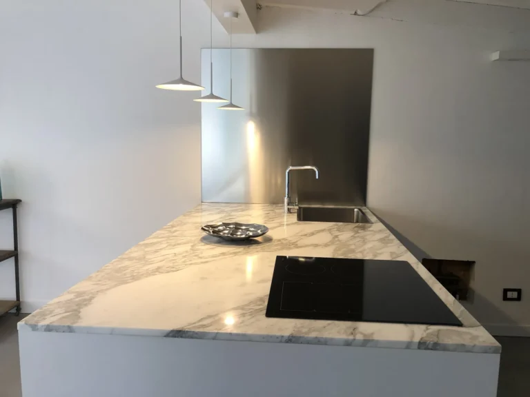 White marble island with induction hob, steel sink and pendant lamps