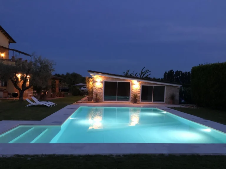 The swimming pool at dusk, with the stone pool house, the olive tree and the villa