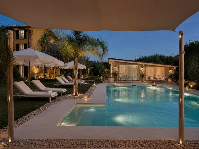 Poolside at dusk under the sail shade: palm tree, white parasols and sun loungers